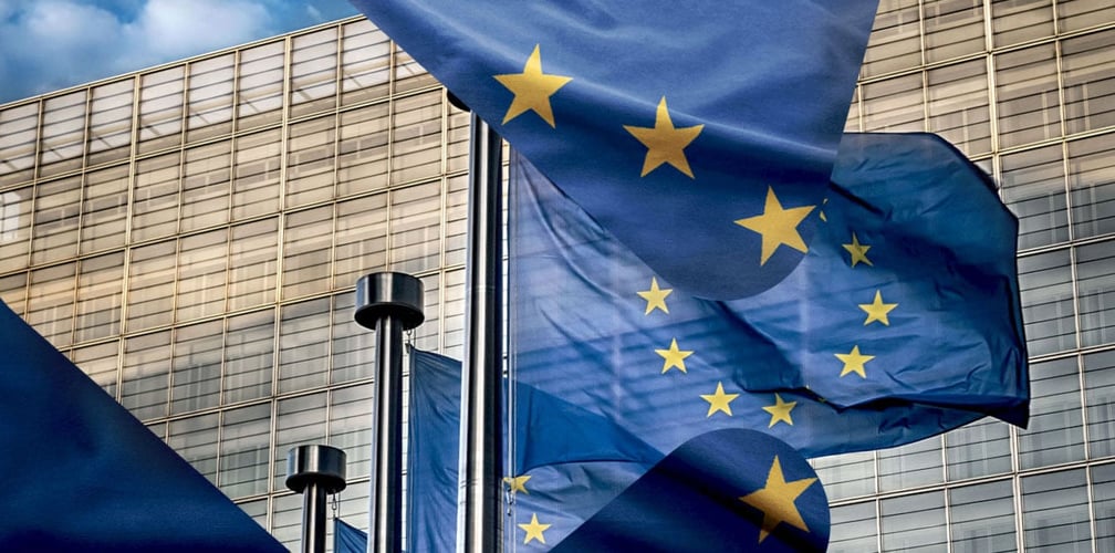 EU flagg som vaier i vinden foran en grå bygning.