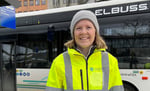 Smilende kvinne med refleksgul jakke står foran elbuss. 