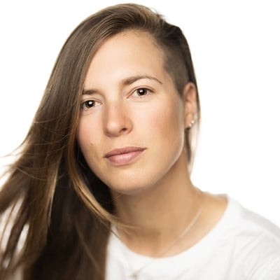 Bilde av Inga Strümke. Hun har langt brunt hår, hvit skjorte og halskjede foran hvit bakgrunn.