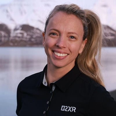 Bilde av Jannicke Mikkelsen. Hun har på seg vart skjorte med Q2XR-logo og står foran snødekte fjell og vann.