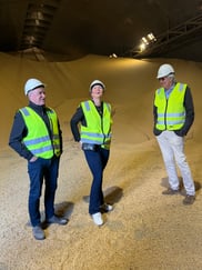 Tre mennesker med refleksvester og vernehatt står i et stort lager av soyabønner