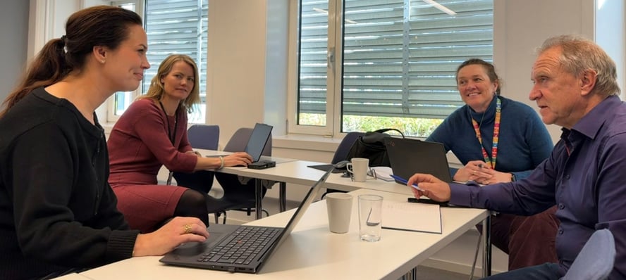 Tre kvinner og en mann sitter med laptoper og diskuterer.