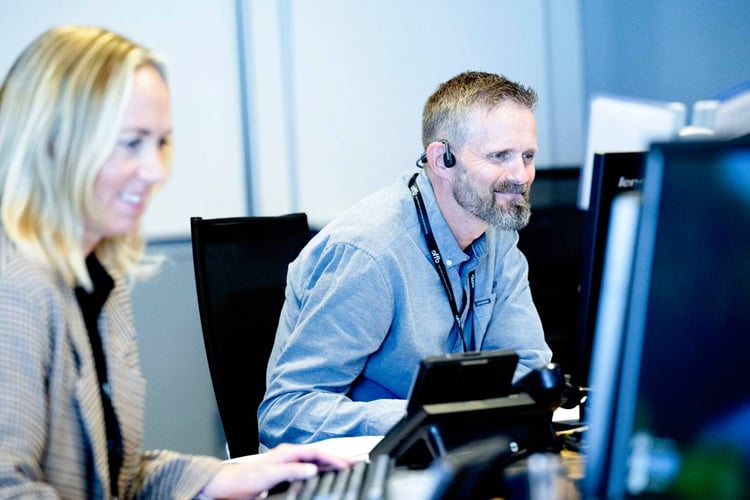 en kvinne og en mann med headset foran pc-skjermer øver på nødsamtaler