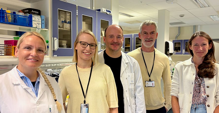 Tre kvinner og to menn i en lab smiler mot kameraet.