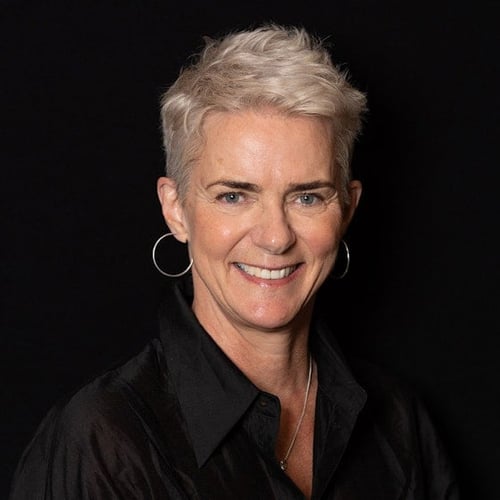 middelaldrende kvinne med kort lyst hår og store ringer i ørene, smiler