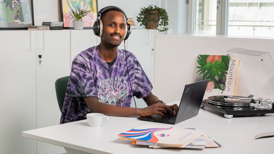 Ung melaninrik man sitter ved en PC og siler mot kamera