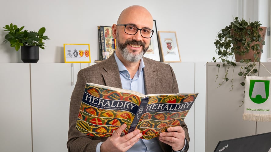 Blid mann med skjegg leser i en bok om heraldikk