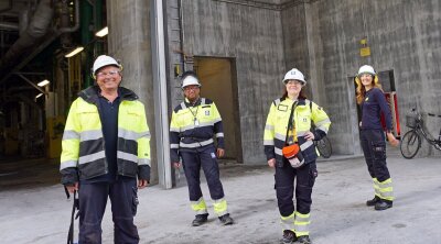 Fire glade anleggsarbeidere i verneutstyr foran inngang til et bygg av betong