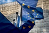 Bilde som er satt sammen av to bilder av blå flagg med gule stjerner i sirkel. EU parlamentet, en høy blokk i stål og glass, er i bakgrunnen
