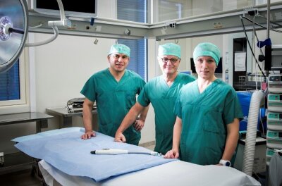 Tre personer i sterile drakter i et operasjonsrom