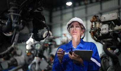 ung kvinne inne i en fabrikk med hjelm og blå kjeldress